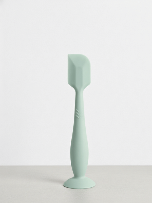 Green 16cm silicone baby bum cream spatula standing upright on its suction base.