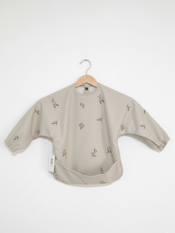 Waterproof long sleeve baby bib apron in cream with an olive branch print and front food catching pocket.